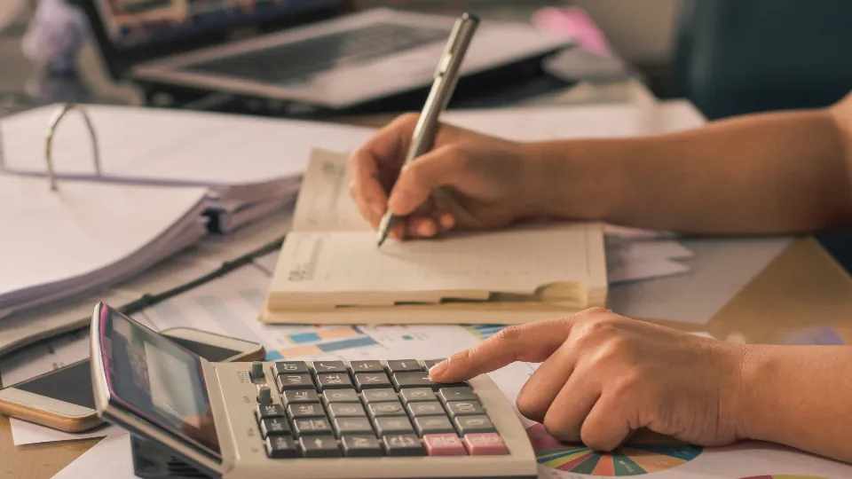Hand working out costs on a calculator next to a notebook