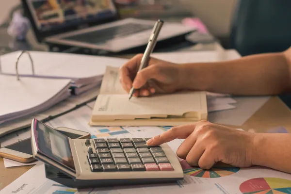 Hand working out costs on a calculator next to a notebook