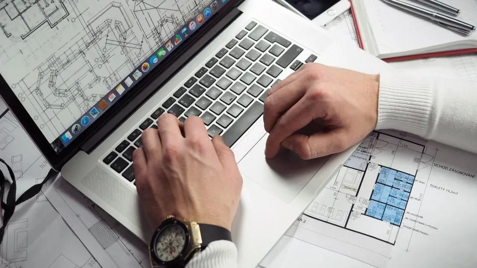 Designer working on a laptop surrounded by printed plans
