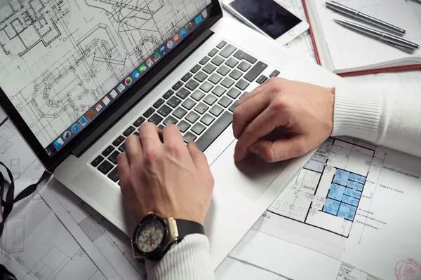 Designer working on a laptop surrounded by printed plans