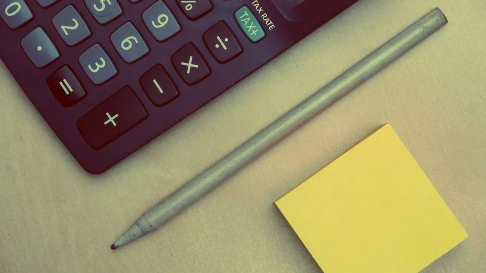Calculator, pencil and sticky note on a desk