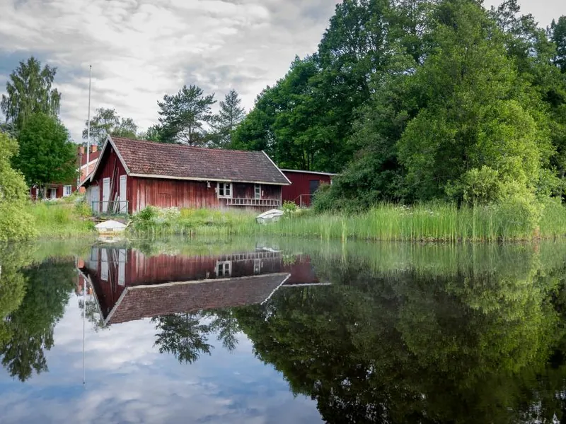Red cottage reflected in a still lake surrounded by trees