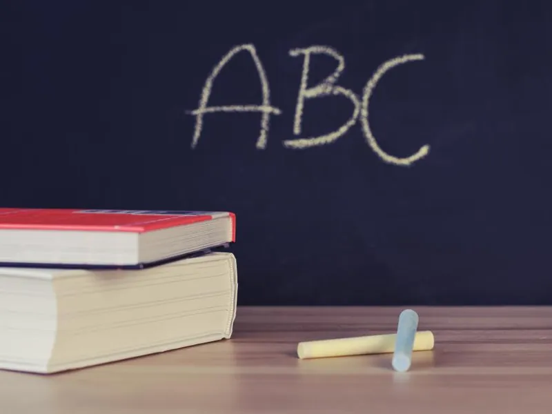 Books on a desk in front of a chalkboard reading ABC