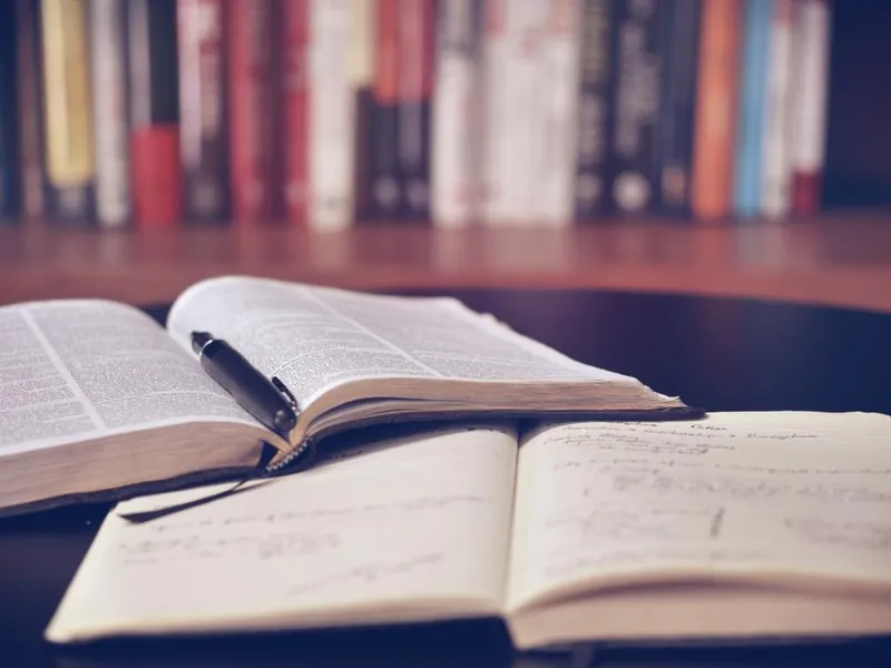 Open books and notebook on a desk in front of a bookshelf