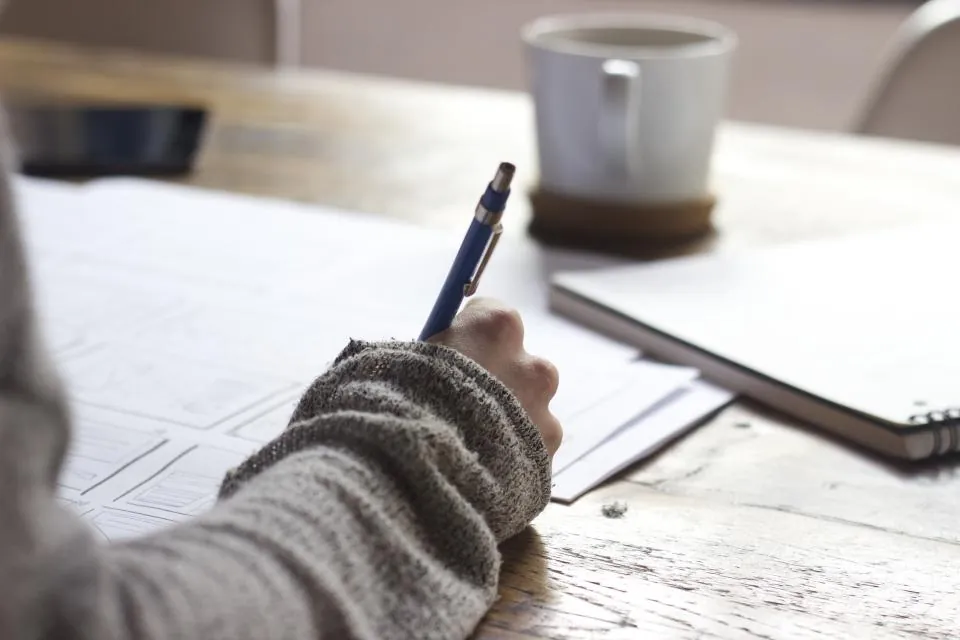 Student writing notes at a desk with a cup of coffee